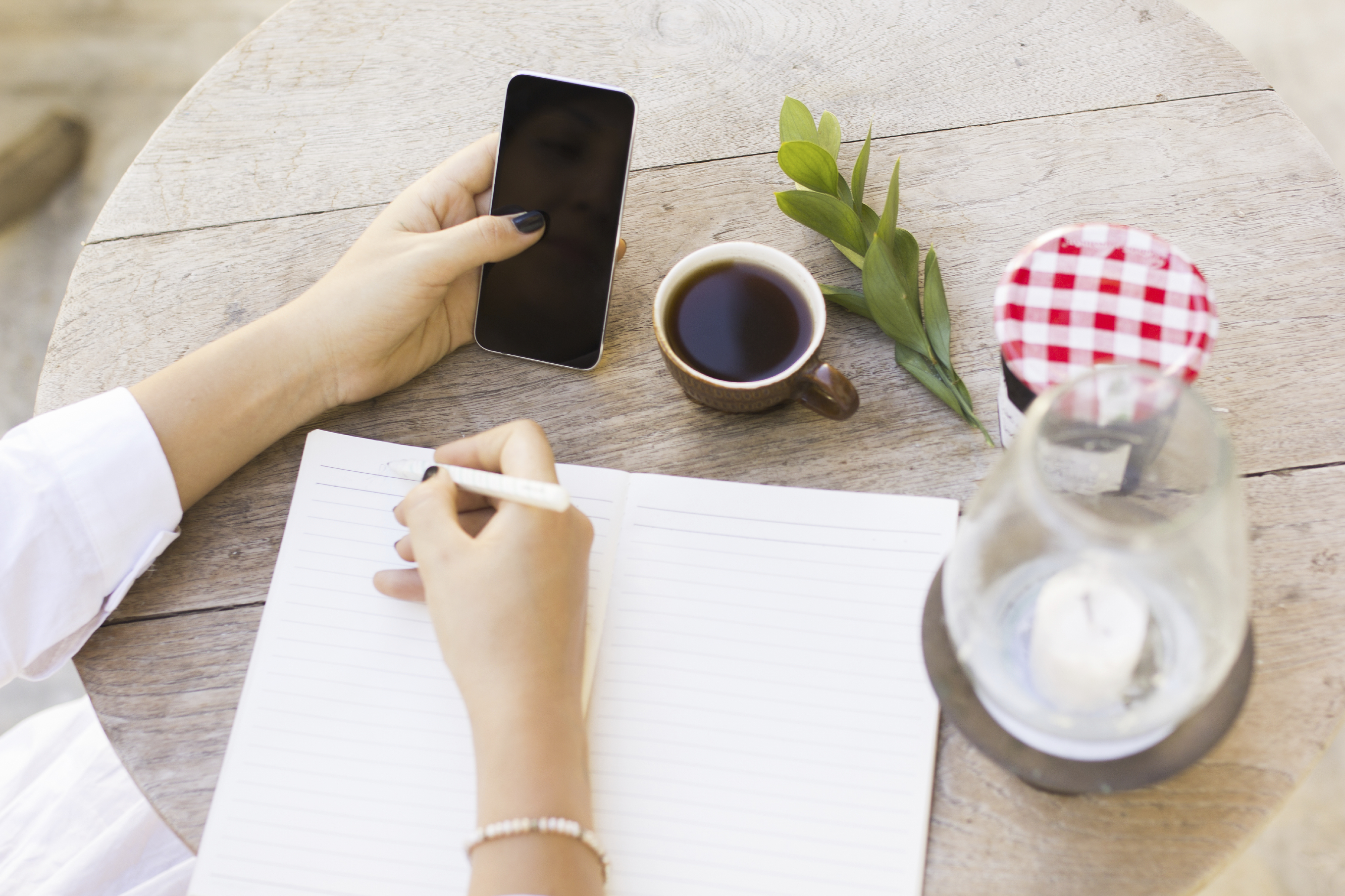 girl writes in notebook with cell phone and cup of coffee