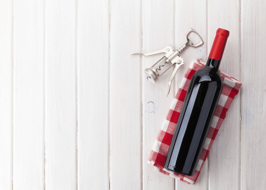 Red wine bottle and corkscrew on white wooden table background with copy space