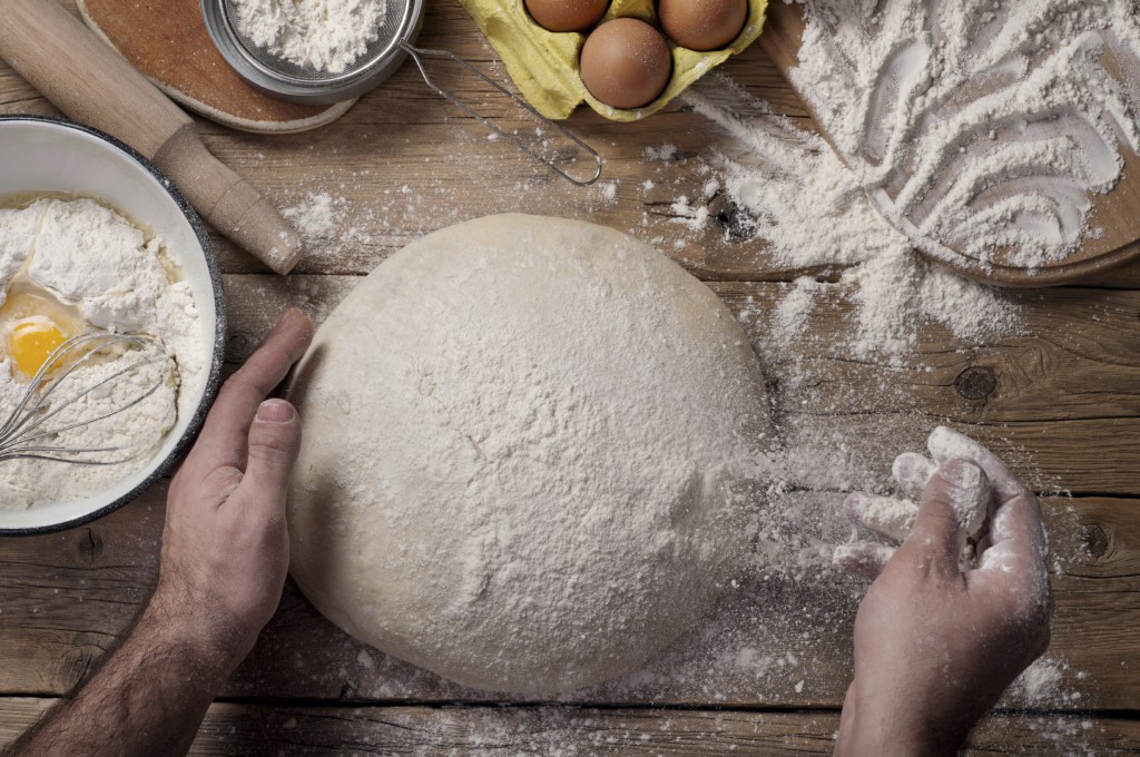 Male baker prepares bread. Male baker sprinkle the dough with flour. Making bread. Top view. Rustic style