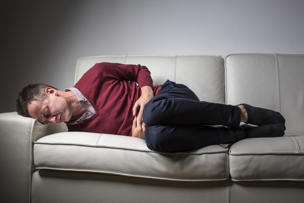 Young man suffering from severe belly pain, being overwhelmed by the debilitating condition of celiac disease/Crohn's disease/strong anxiety