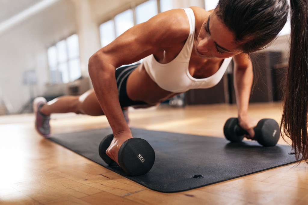 Gym woman doing push-up exercise with dumbbell. Strong female doing gym workout.