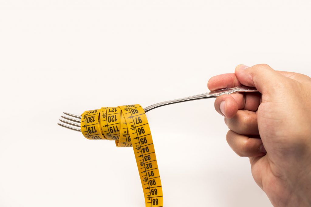 hand holding a fork with a tape measure for diet concept