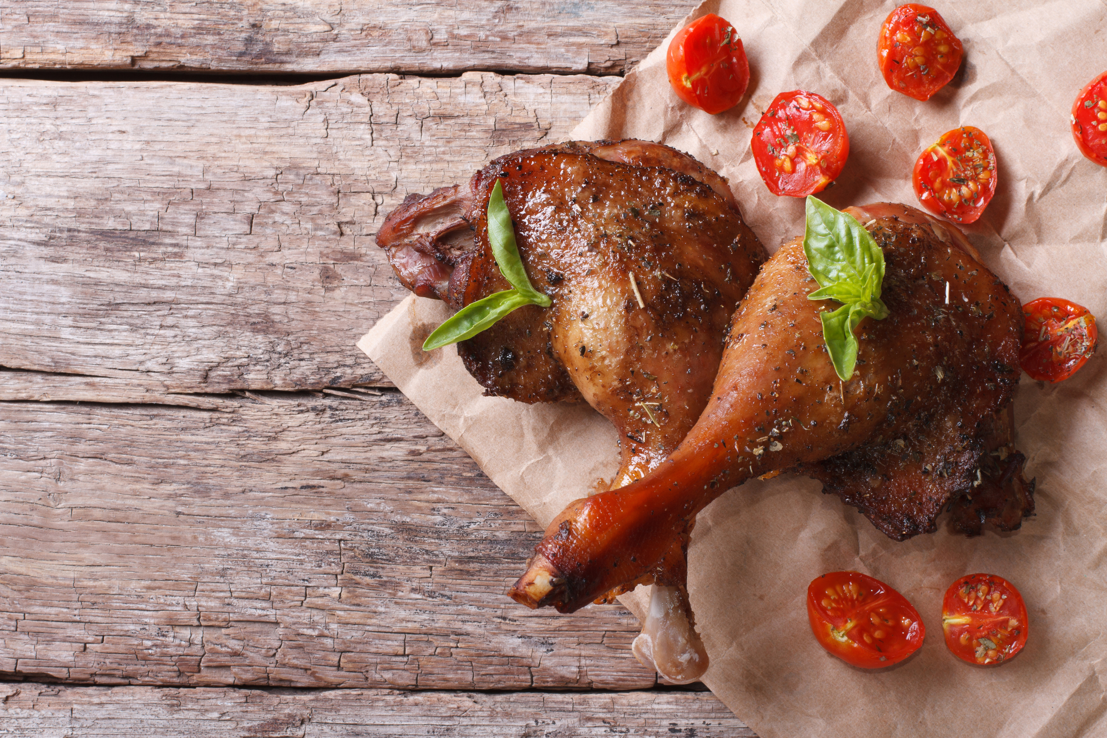 two roasted duck legs with basil and tomatoes close up on an old table top view horizontal